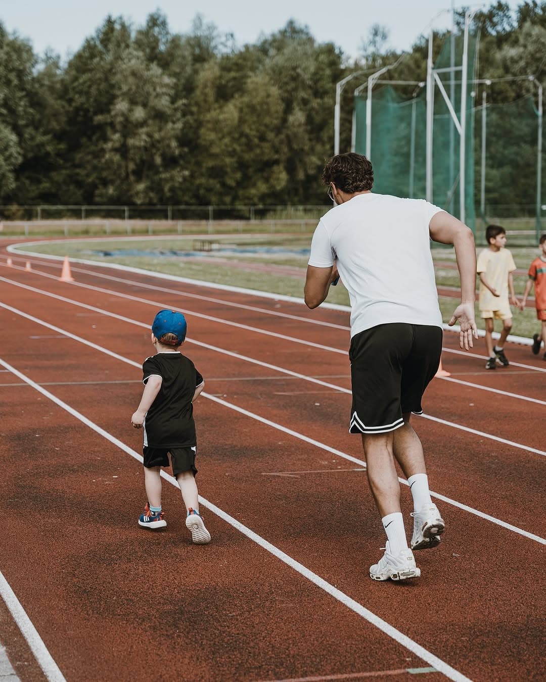 Begeleider loopt mee met kind op de atletiekbaan tijdens de Eid Adha Sportdag